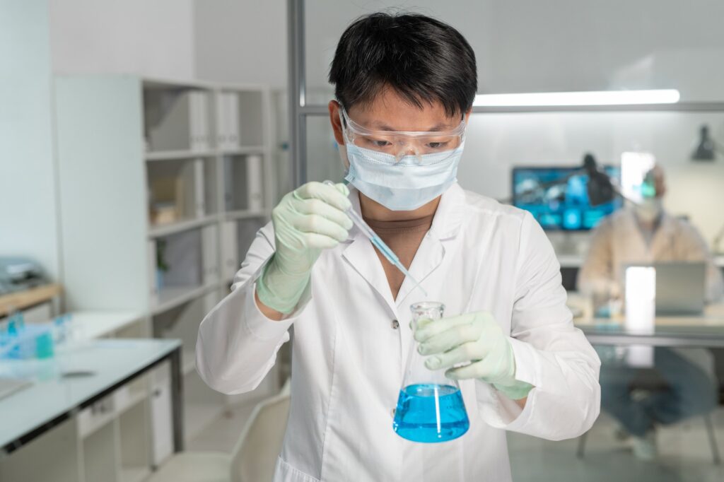 Young Asian female chemist adding drop of chemical substance into blue liquid