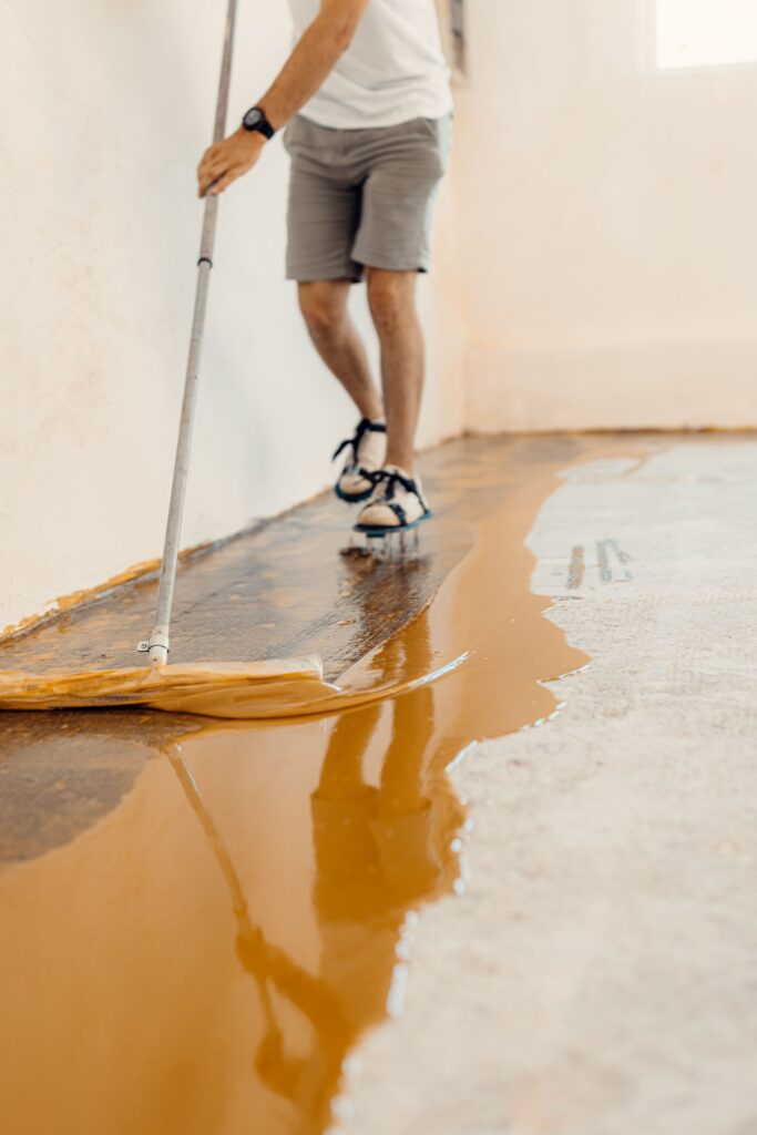 Closeup shot of a handyman applying yellow liquid paint on a new floor