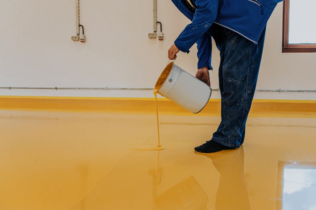 Worker, coating floor with self-leveling epoxy resin in industrial workshop.