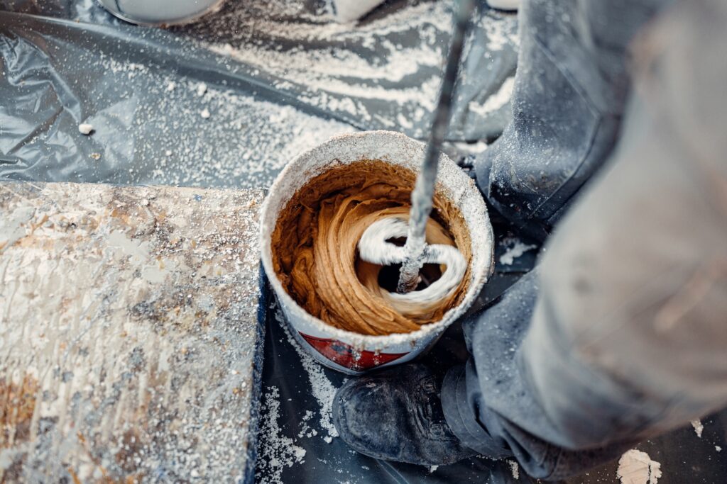 Professional worker mixes two chemical compounds in the metal bucket using the mixer